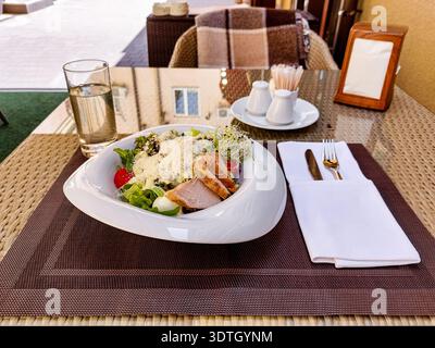 Salade César au poulet sur la terrasse extérieure ensoleillée – déjeuner gastronomique frais, table de restaurant confortable, style de vie sain, lumière du jour chaude, ambiance calme Banque D'Images