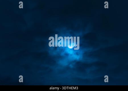 Pleine lune brillante à travers des nuages sombres dramatiques dans Deep Blue Night Sky. Une vue fascinante d'une pleine lune brillante partiellement obscurcie par des nuages sinueux Banque D'Images