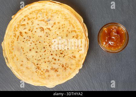 Crêpes sucrées sur une pierre d'ardoise avec confiture, vue de dessus, macro. Banque D'Images