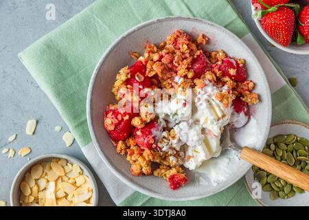 Crumble de fraise dessert avec crème glacée à la vanille fondante, granola cuit au four, graines de citrouille et amandes dans un bol avec cuillère sur fond gris. Fait maison Banque D'Images