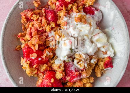 Crumble aux fraises avec crème glacée fondante, granola cuit au four, graines de citrouille et amandes dans un bol. Dessert aux fruits croustillants d'été. Pâtisserie sucrée maison avec Banque D'Images