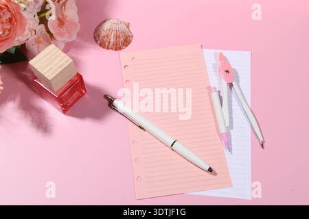 Parfum, stylo et papier à notes vierges lignées. Boussole et coquillage sur surface rose. Banque D'Images