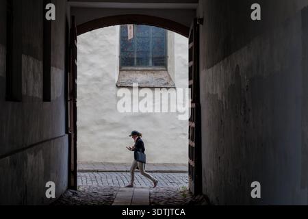 Une personne solitaire marchant devant une ancienne arche en pierre dans la vieille ville médiévale de Tallinn, en Estonie, silhouette contre un vitrail Banque D'Images