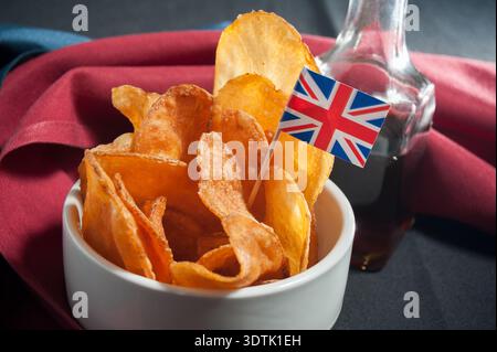 Croustillantes de pub de style britannique servies dans un bol blanc, avec une bouteille de vinaigre de malt foncé à côté. Un petit drapeau britannique ajoute une touche d'authenticité Banque D'Images
