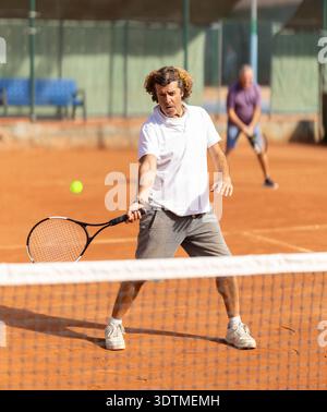 Deux hommes en vêtements de sport jouant au paddle tennis couple match sur des courts de tennis, joueur masculin recevant le coup de la raquette de tennis Banque D'Images