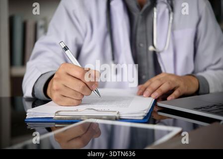 Médecin écrit à la main sur le presse-papiers médical, remplissant le formulaire du patient à la clinique. Médecin en manteau blanc avec stéthoscope écrivant la prescription, travaillant avec Banque D'Images