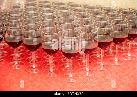Des dizaines de verres à vin rouge remplis et disposés en rangées précises sur une nappe rouge, préparés pour une réception ou une dégustation. Visuel idéal pour la restauration, ho Banque D'Images