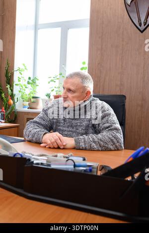 Homme caucasien senior avec les cheveux gris est assis à un bureau, concentré et triste, travaillant sur un ordinateur. Banque D'Images