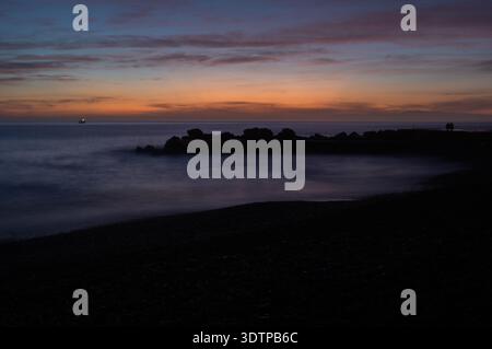 Coucher de soleil sombre sur la côte avec mer et silhouette rocheuse sous ciel orange dramatique Banque D'Images