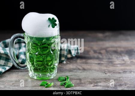 Mug de bière vert versant avec mousse pour la fête de Patrick sur table en bois noir et fond noir Banque D'Images