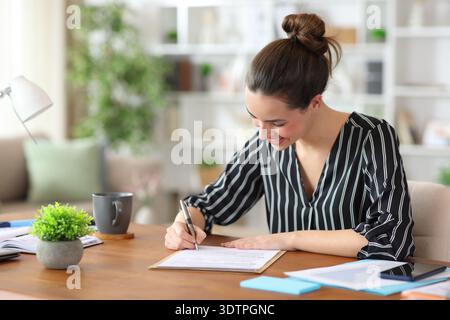 Heureux travailleur indépendant signant un document papier travaillant à la maison Banque D'Images