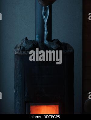 De l'eau est versée sur des charbons sur un sauna tiré au feu de bois en Suède Banque D'Images
