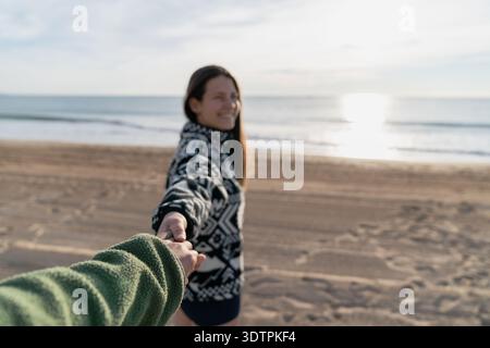 Femme souriante tenant la main sur la plage au lever du soleil Banque D'Images