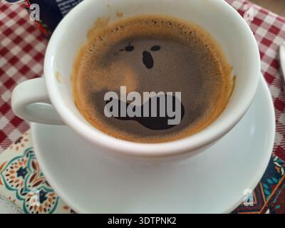 Tasse de café expresso sur soucoupe avec surface de crème ressemblant à un visage surpris, gros plan sur la table Banque D'Images