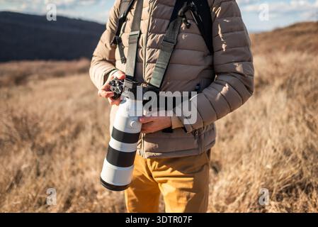Gros plan d'un photographe en plein air au milieu des prairies sèches, à l'aide d'un objectif zoom long pour photographier la nature par temps clair. Banque D'Images