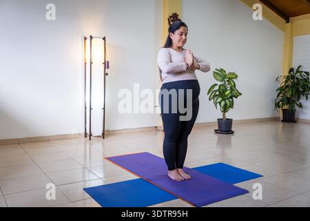 Femme enceinte debout sur un tapis de yoga avec les mains ensemble dans un studio Banque D'Images
