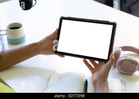 La tablette est tenue horizontalement sur une table blanche, avec un ordinateur portable, un stylo, une tasse, un casque Banque D'Images