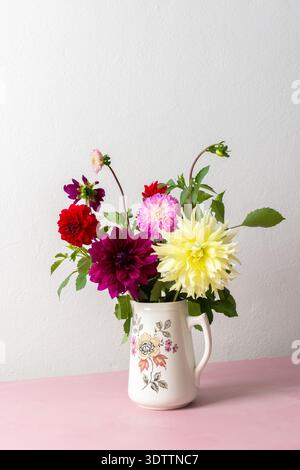 Un vase contient une variété de fleurs fraîches avec différentes couleurs. Les fleurs sont placées sur une table rose. Derrière le vase se trouve un mur Uni dans un roo lumineux Banque D'Images