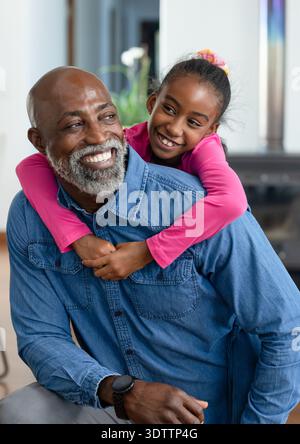 Homme senior afro-américain et fille enfant assis tout en se penchant, serrant à la maison avec chemise en Jean Banque D'Images