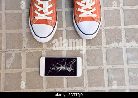 Personne ramassant le téléphone intelligent cassé avec l'écran fissuré du sol Banque D'Images