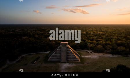 Vue aérienne de l'ancienne pyramide maya El Castillo se dresse majestueusement au milieu d'une mer de jungle verte, sous un ciel chaud et doré de coucher de soleil, Chichén-I. Banque D'Images