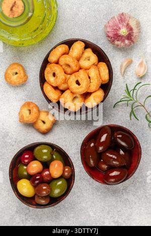 Tarallini-petits bagels italiens traditionnels. Taralli. Collation savoureuse. Olives noires et vertes, Kalamata, huile d'olive, ail et romarin sur béton gris Banque D'Images