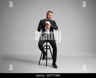 Homme assis sur une chaise dans un studio et ajustant les boutons de manchette sur sa manche Banque D'Images