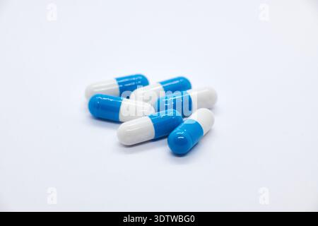 Un gros plan, en grand angle, de plusieurs capsules pharmaceutiques bicolores bleues et blanches, contenant probablement des médicaments ou des suppléments, dispersées sur un c Banque D'Images