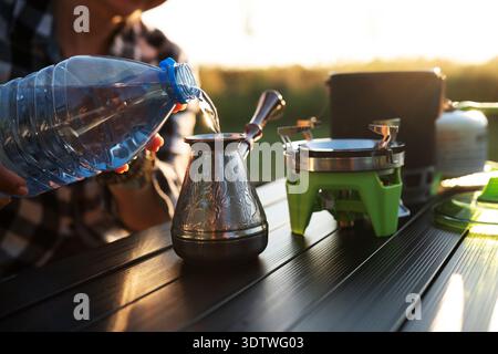 Femme faisant du café dans Un Cezve sur Un poêle de camping portable et versant de l'eau dans Un pot turc Banque D'Images