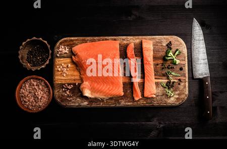 filet de poisson rouge de saumon avec des herbes prêtes pour la cuisson d'un dîner sain sur une table noire, vue de dessus Banque D'Images