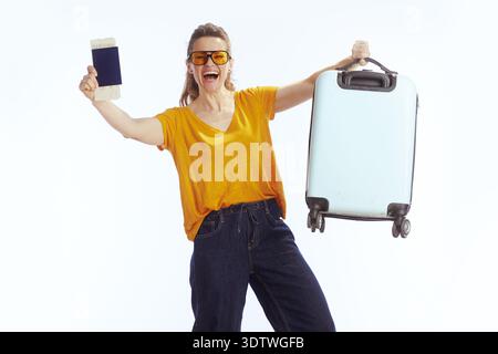 Une voyageuse excitée portant des lunettes de soleil jaunes se tient debout avec sa valise, tenant un passeport et des cartes d'embarquement tout en encourageant son prochain summe Banque D'Images