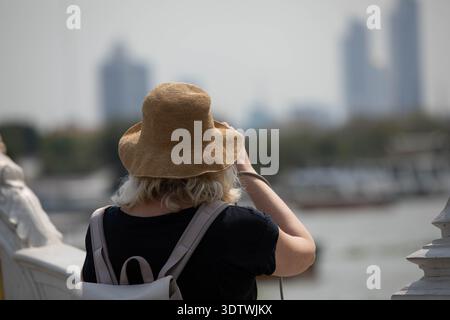 Femme senior en t-shirt noir et chapeau tricoté marron marchant en prenant des photos à la jetée, vue arrière, à la jetée Wat Rakhang. Banque D'Images