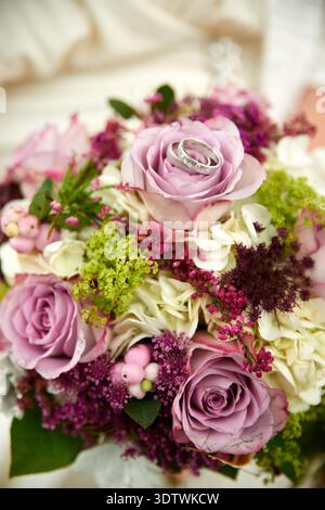 Un gros plan romantique d'un bouquet de mariée vibrant, mettant en vedette deux élégantes bagues de mariage en argent avec des accents de diamant délicatement placés sur une esclave proéminente Banque D'Images