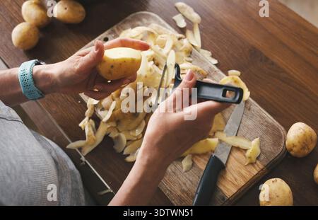 Vue de dessus d'Une femme épluchant des pommes de terre crues avec Un éplucheur de pommes de terre et d'autres légumes crus Banque D'Images
