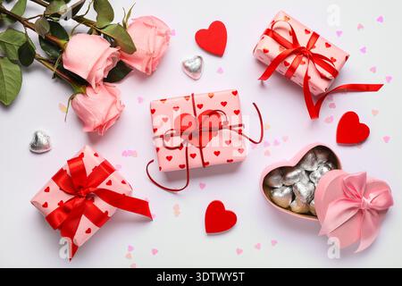 Boîtes cadeaux avec bonbons, coeurs décoratifs et fleurs roses sur fond blanc. Célébration de la Saint-Valentin Banque D'Images