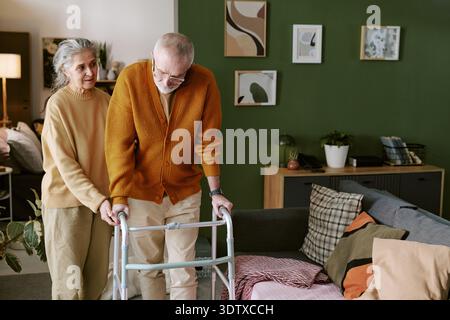 Femme caucasienne senior aidant homme caucasien senior utilisant Walker à l'intérieur Banque D'Images