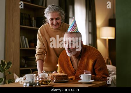 Homme caucasien senior soufflant la bougie sur le gâteau d'anniversaire avec femme senior souriant Banque D'Images