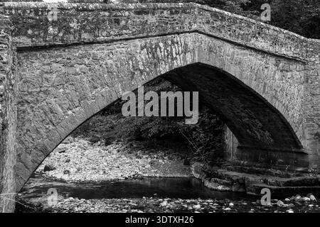 Vue en noir et blanc sur l'ancien pont de cheval de bataille en pierre traversant la rivière Cover Banque D'Images