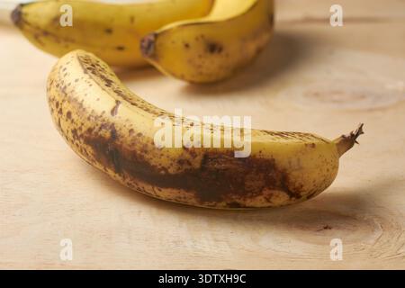 banane jaune surmûre sur une surface en bois texturée claire, fruits avec des taches de peau noire, gros plan doux avec espace de copie, sensibilisation au gaspillage alimentaire Banque D'Images