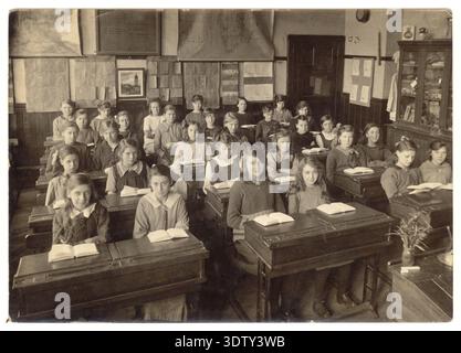 1900s ,1920s écoliers, classe de filles de l'école junior assis à des bureaux, livres ouverts dans la classe des années 1900, ayant une leçon, 1920's School Children UK Banque D'Images