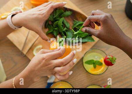 Mains cueillant la menthe fraîche et garnissant les boissons aux agrumes sur la table en bois, lumière vive Banque D'Images