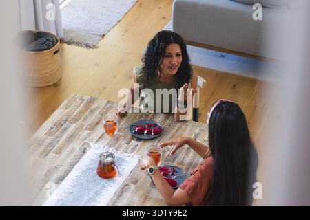 Théière en verre trempant le thé ambre avec deux verres sur la table à manger en bois dans la maison, desserts rouges Banque D'Images