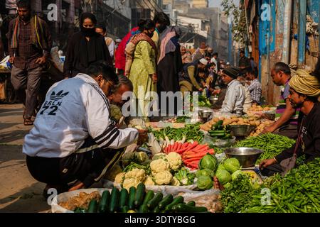 Divers légumes frais exposés dans un marché de rue dans le vieux Delhi. Les gens achètent des produits, avec plus de stands visibles au loin. Banque D'Images