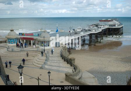 Une vue aérienne de la ville côtière de Cromer, Norfolk, située sur la côte de la mer du Nord. La perspective met en évidence l'architecture victorienne, l'église Saint-Pierre et Saint-Paul du XIVe siècle avec sa tour de 160 pieds, et la jetée classée Grade II, qui a ouvert ses portes en 1901. Historiquement un petit village de pêcheurs connu pour son 'crabe Cromer', la ville s'est développée en une station balnéaire populaire à la fin du XIXe siècle après l'arrivée du Great Eastern Railway. La vue englobe le paysage de falaise, les plages de sable et la disposition dense du centre-ville historique. Banque D'Images