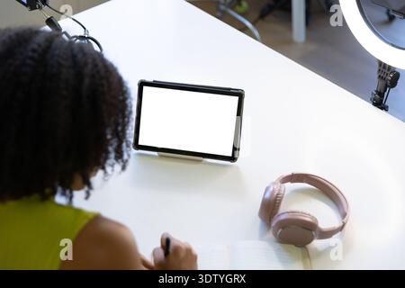 La tablette affiche un écran blanc vierge sur le socle tandis que les écouteurs roses reposent sur le bureau blanc Banque D'Images