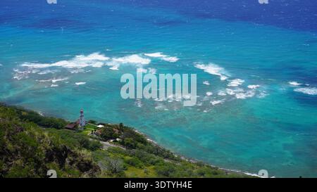 Vue sur l'océan turquoise et le récif corallien depuis Diamond Head à Honolulu, Hawaï, avec le phare de Diamond Head visible sur la colline. Les vagues se brisent au-dessus de t Banque D'Images