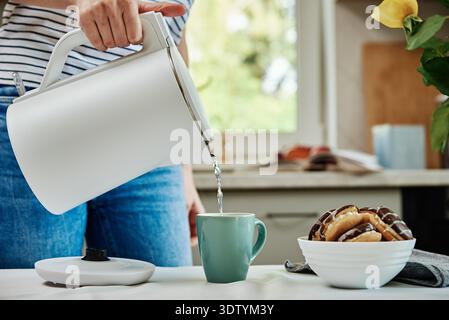 Temps du thé, femme versant de l'eau bouillie de la bouilloire électrique dans la tasse pour préparer le thé, petit déjeuner dans la cuisine Banque D'Images