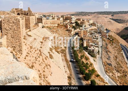 Vue du château de Kerak en Jordanie avec des maisons à proximité. Une route sinueuse traverse le terrain rocheux et montre les collines lointaines. Banque D'Images