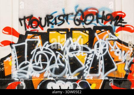 Graffiti coloré sur un mur dans la ville de Catane, Sicile, Italie, avec un message disant "Tourist Go Home". Banque D'Images