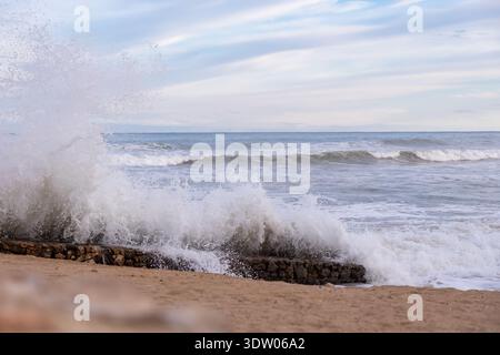 Une puissante vague s'écrase contre un brise-lames en pierre sur la côte méditerranéenne de l'Espagne, capturant la force brute de la nature dans une scène côtière dynamique. Banque D'Images